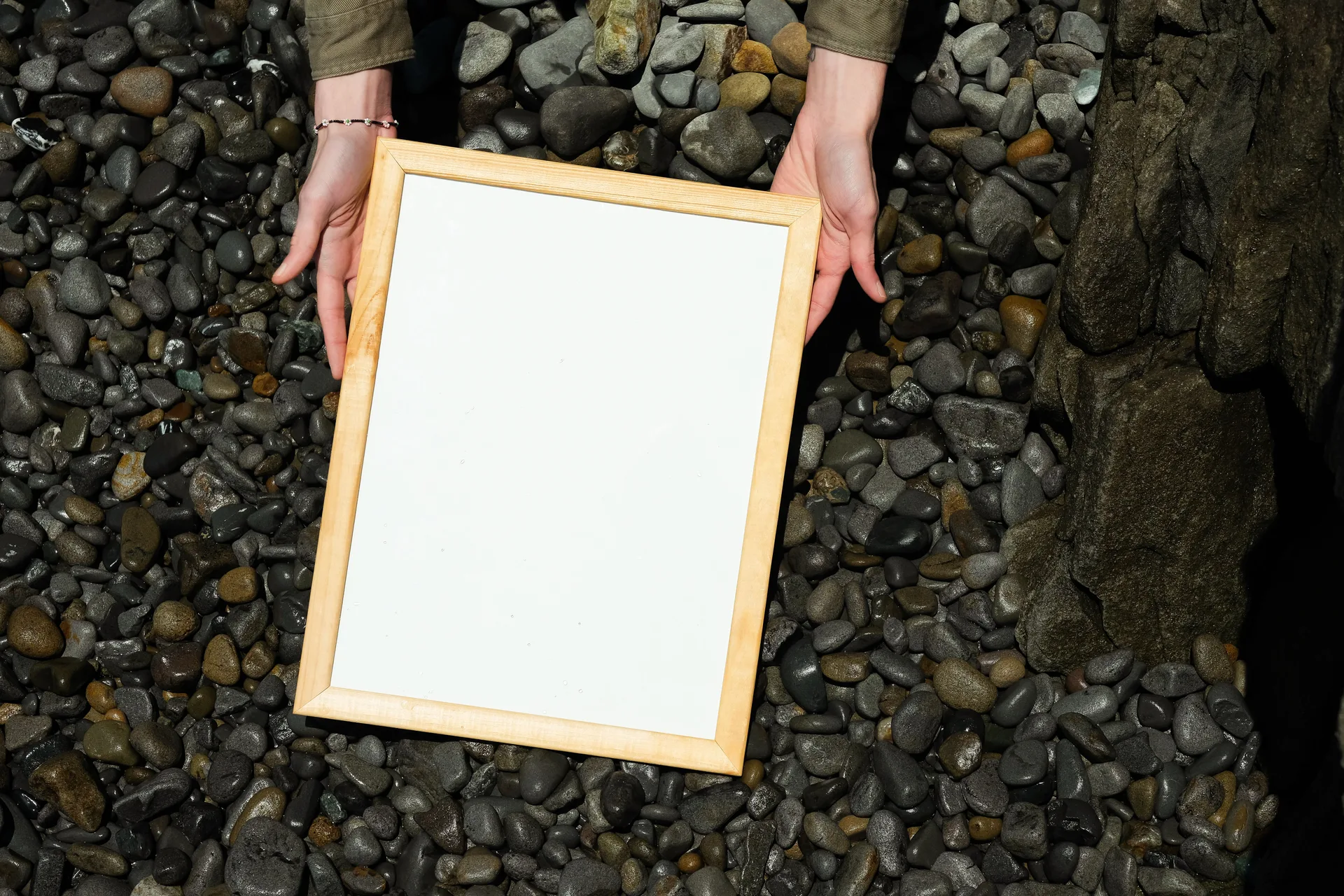 Hands holding an empty wooden picture frame over river stones, representing a still image captured from video